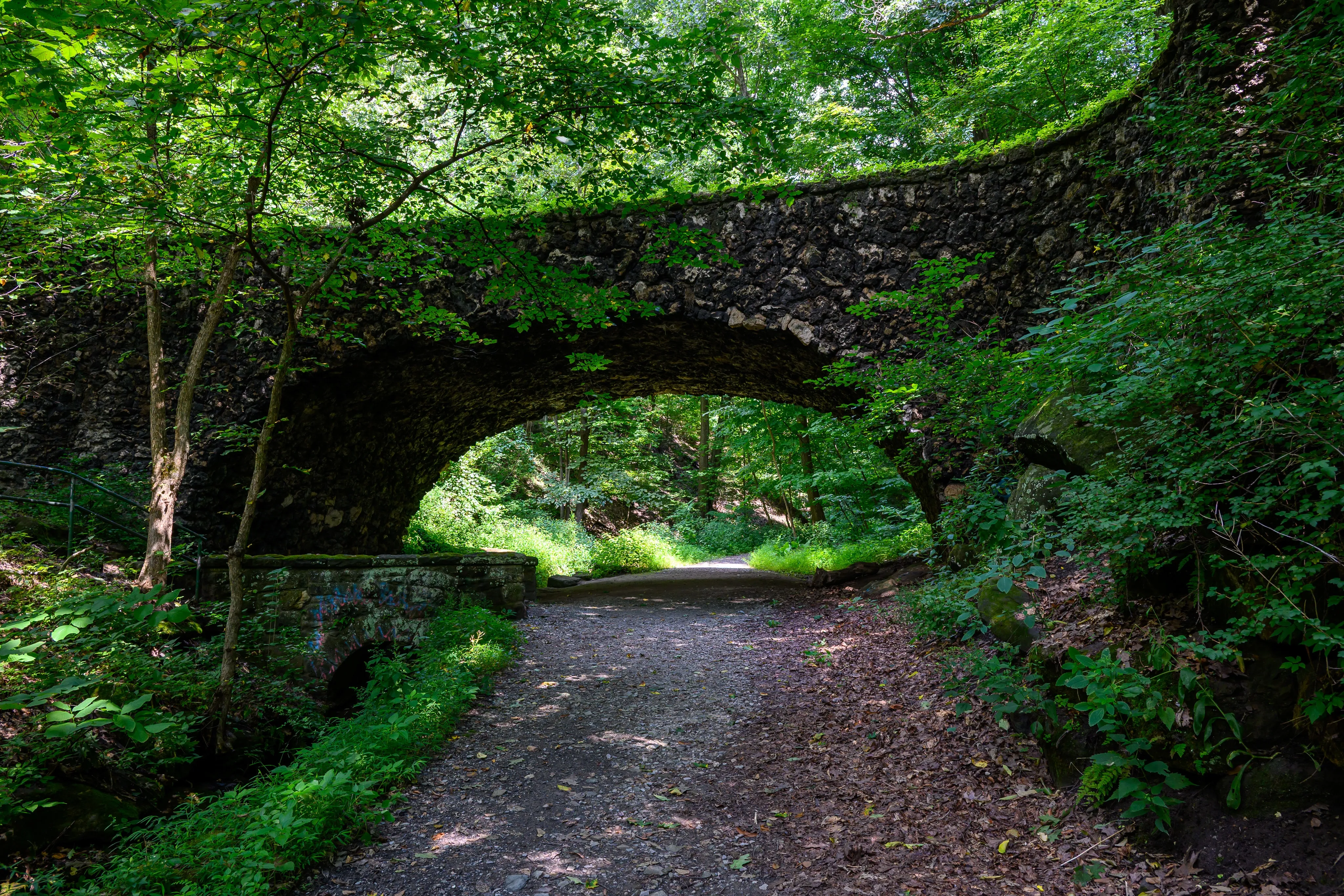 A stone footbridge arching over a wooded park trail.