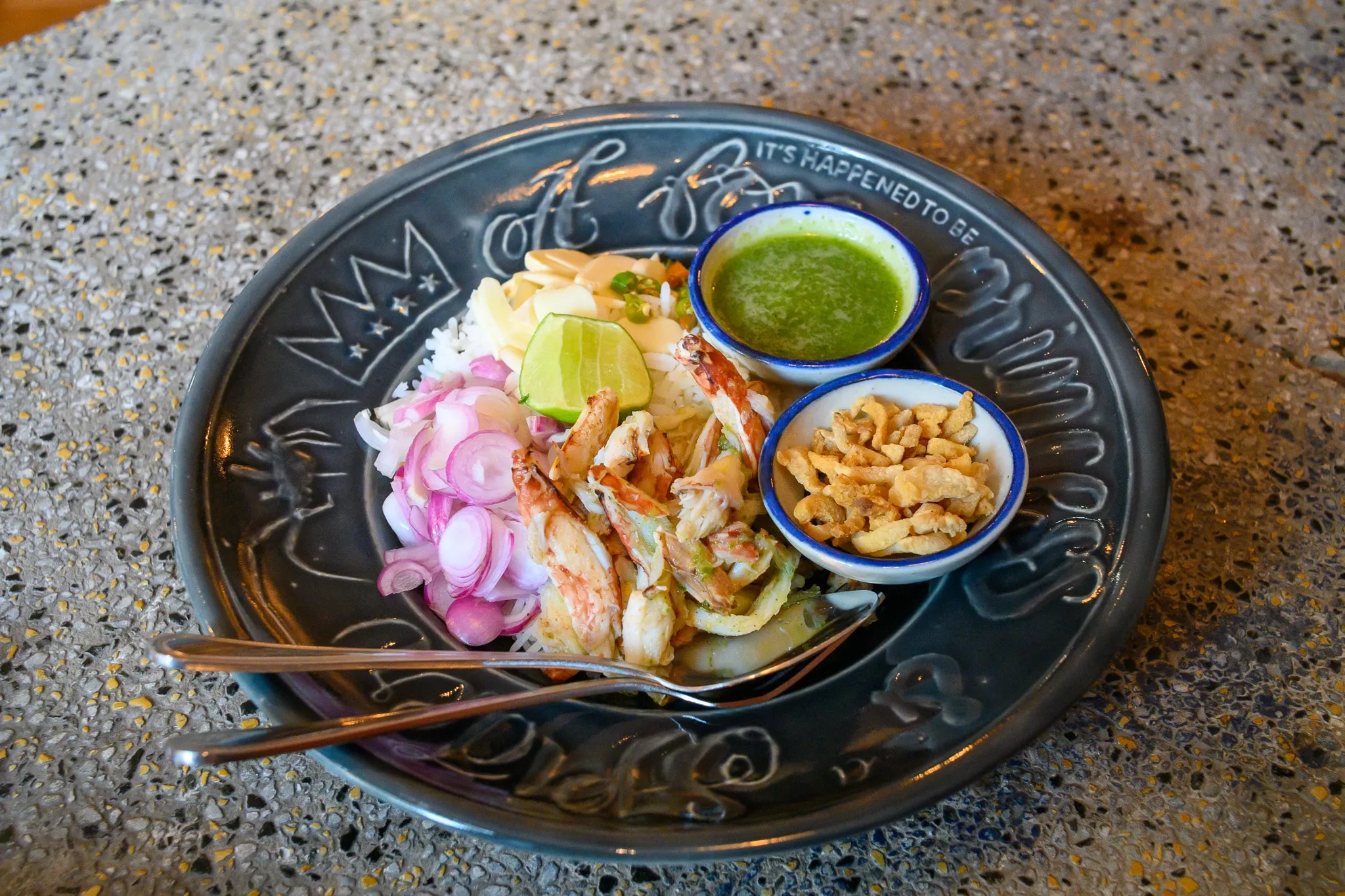 A crab and rice dish with pickled shallots, lime, and dipping sauces on a dark plate