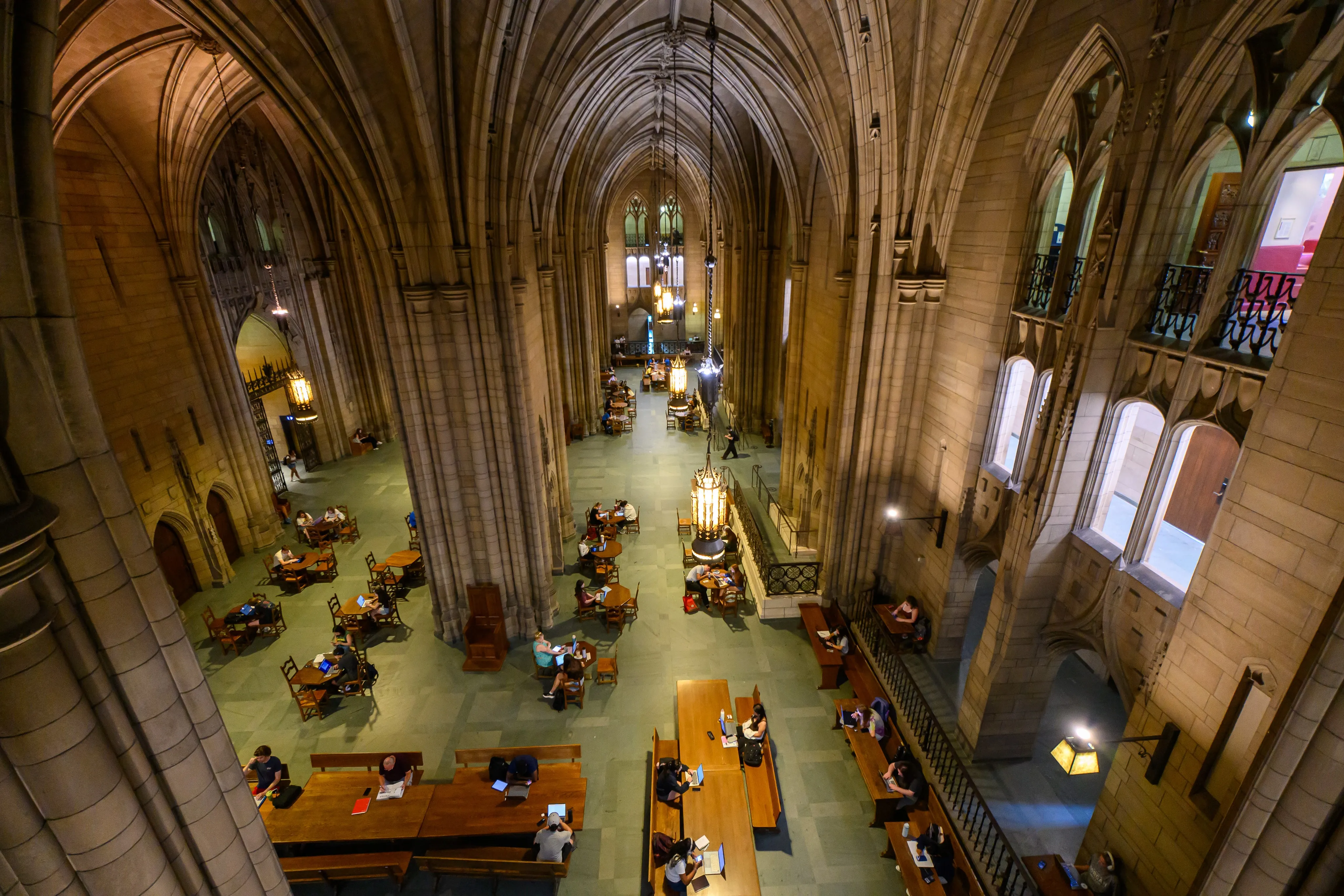 An overhead view of a Gothic vaulted study hall with students seated at long wooden tables.