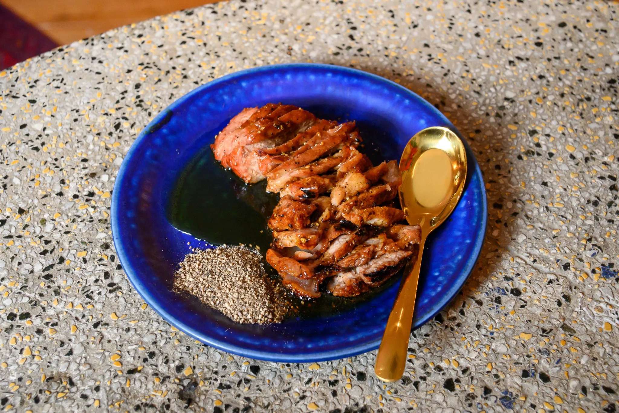 Grilled glazed pork with a pepper dip on a cobalt-blue plate with a gold spoon