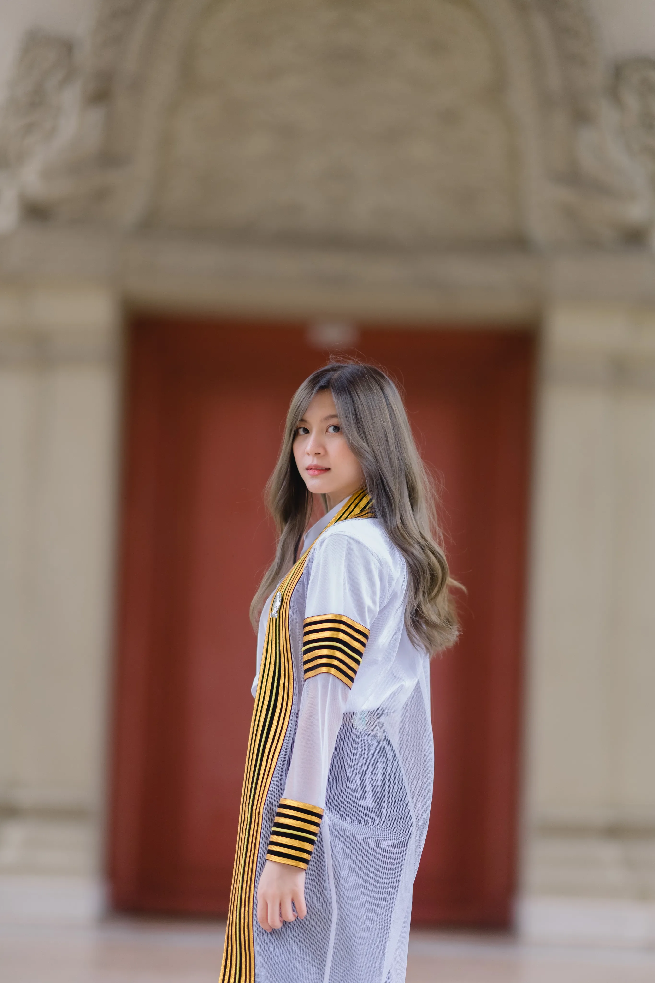 A graduate in a striped academic gown looking back over her shoulder in front of a red door