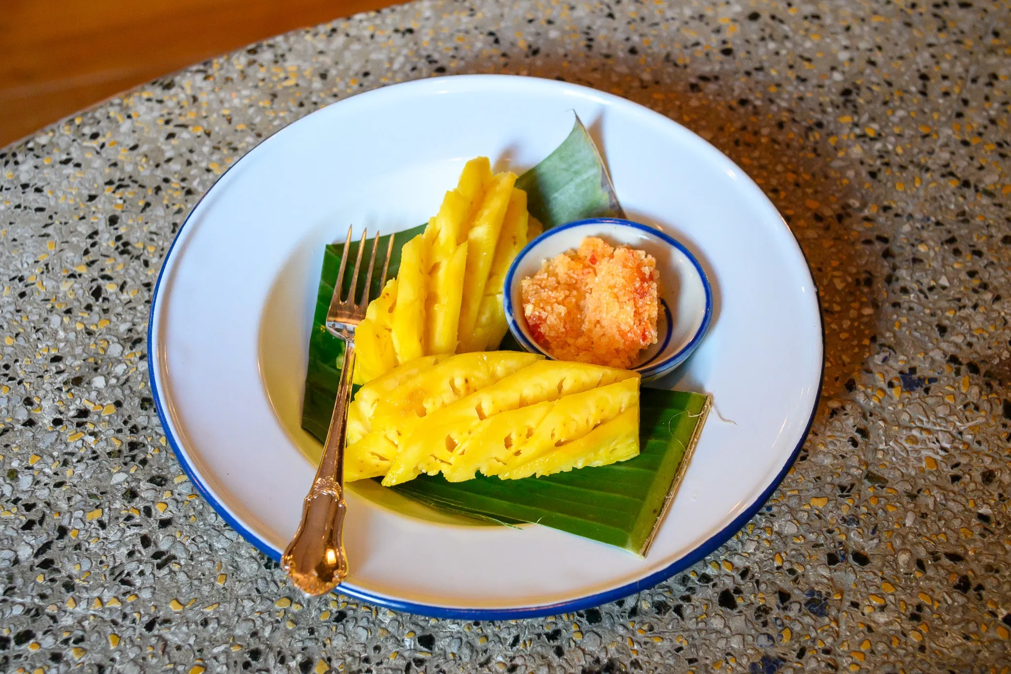 Sliced pineapple on a banana leaf with a small bowl of salted dip