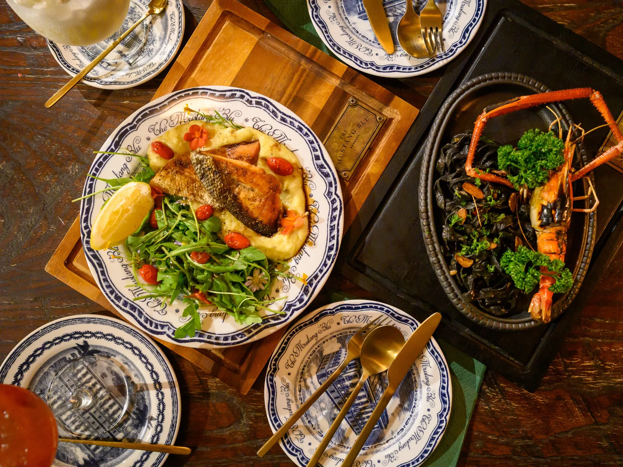 A table set with seared fish on mashed potato, a salad, and grilled prawns with black pasta