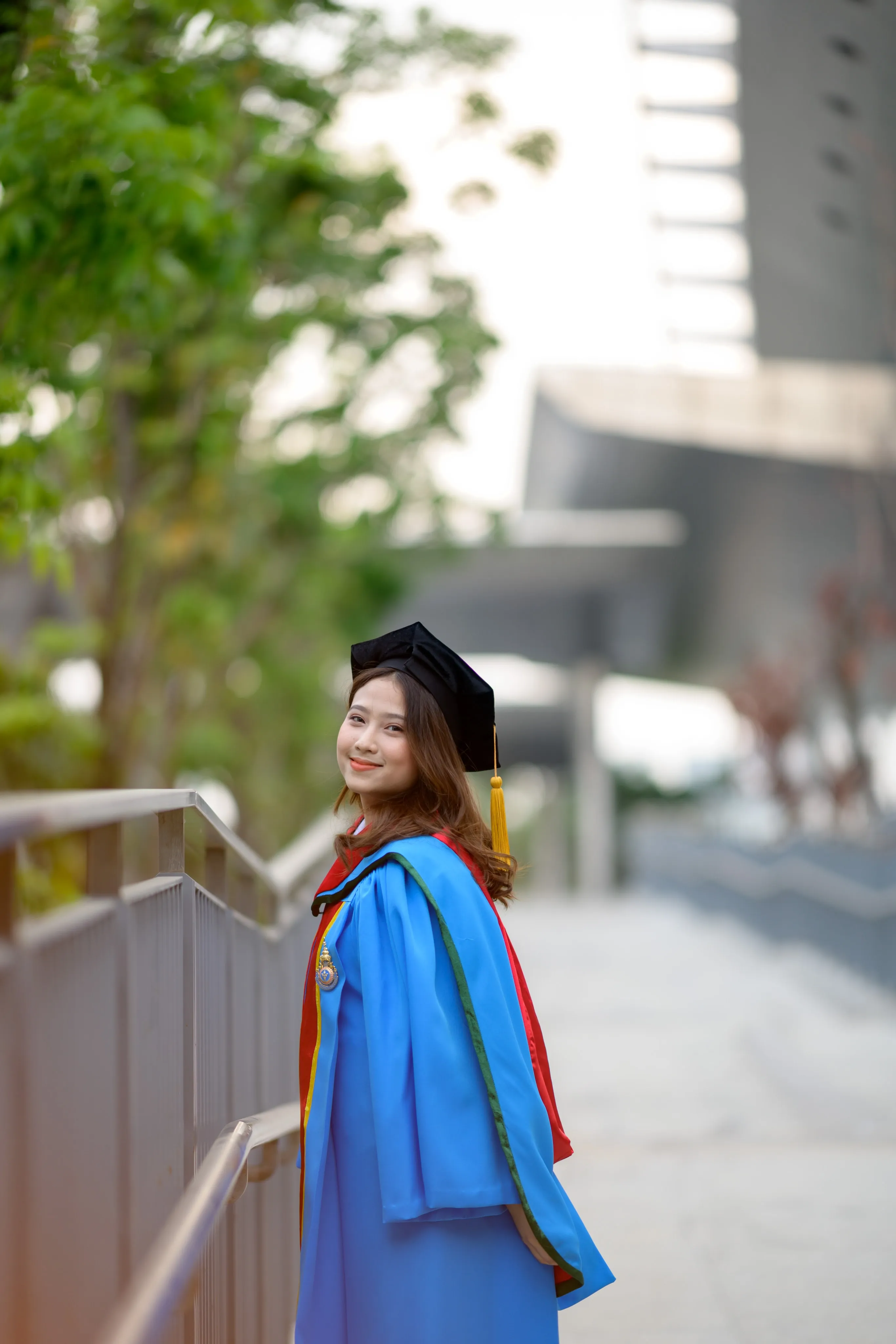 A graduate in a mortarboard and blue gown looking back along a walkway railing