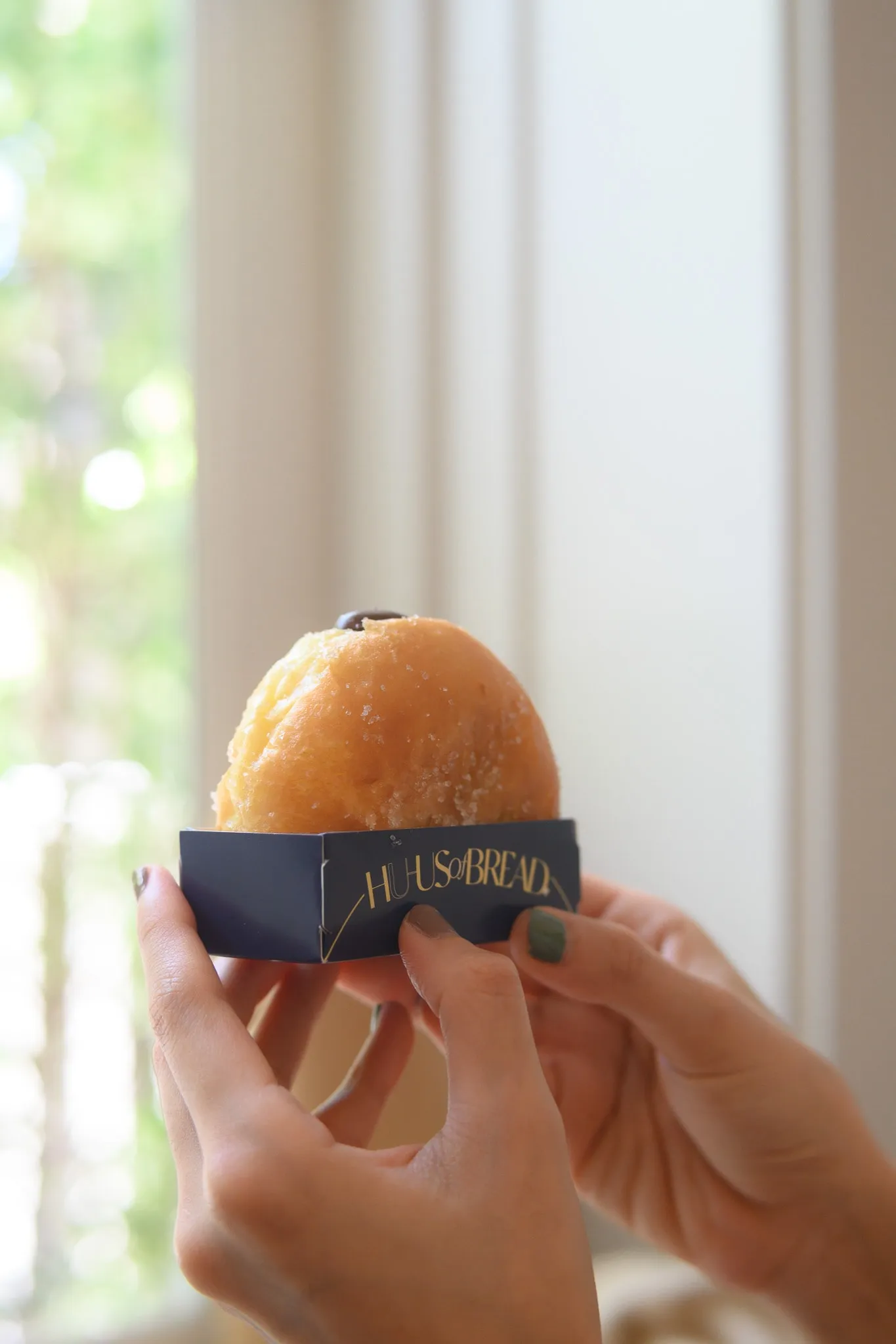 Hands holding up a sugar-dusted brioche doughnut in a branded paper sleeve