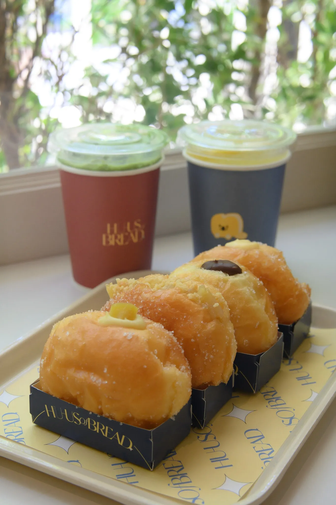 A row of filled brioche doughnuts on a tray in front of two branded drink cups