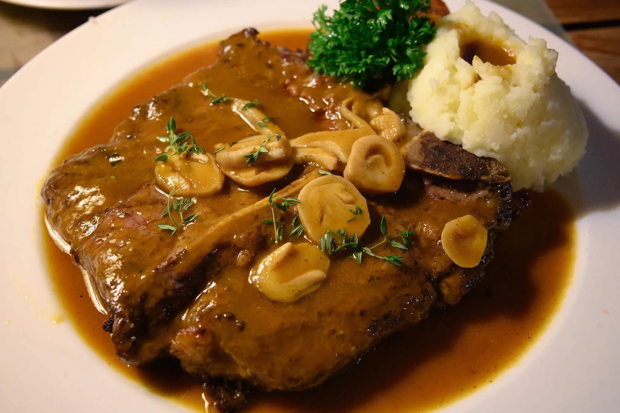 A pork chop in mushroom gravy with mashed potato and parsley