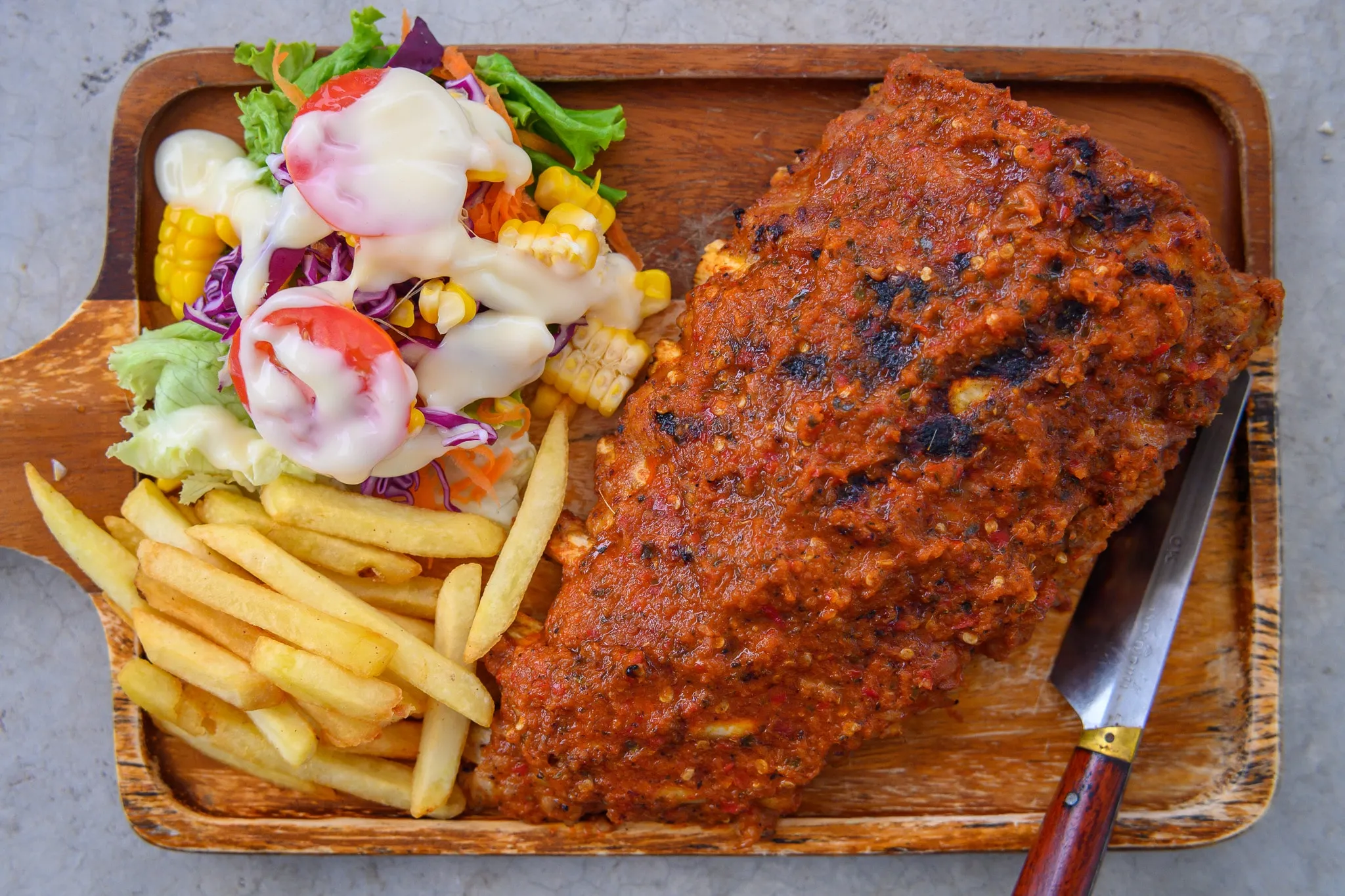 A spice-rubbed grilled steak with fries and a salad on a wooden board