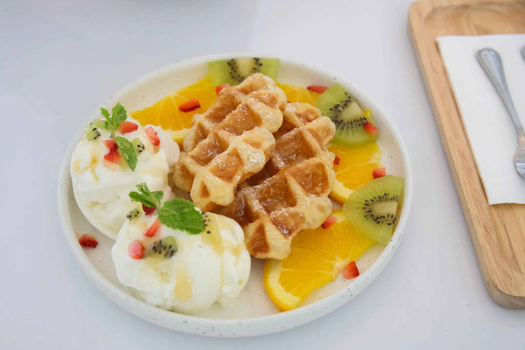 Waffles with scoops of ice cream, orange slices, and kiwi on a white plate