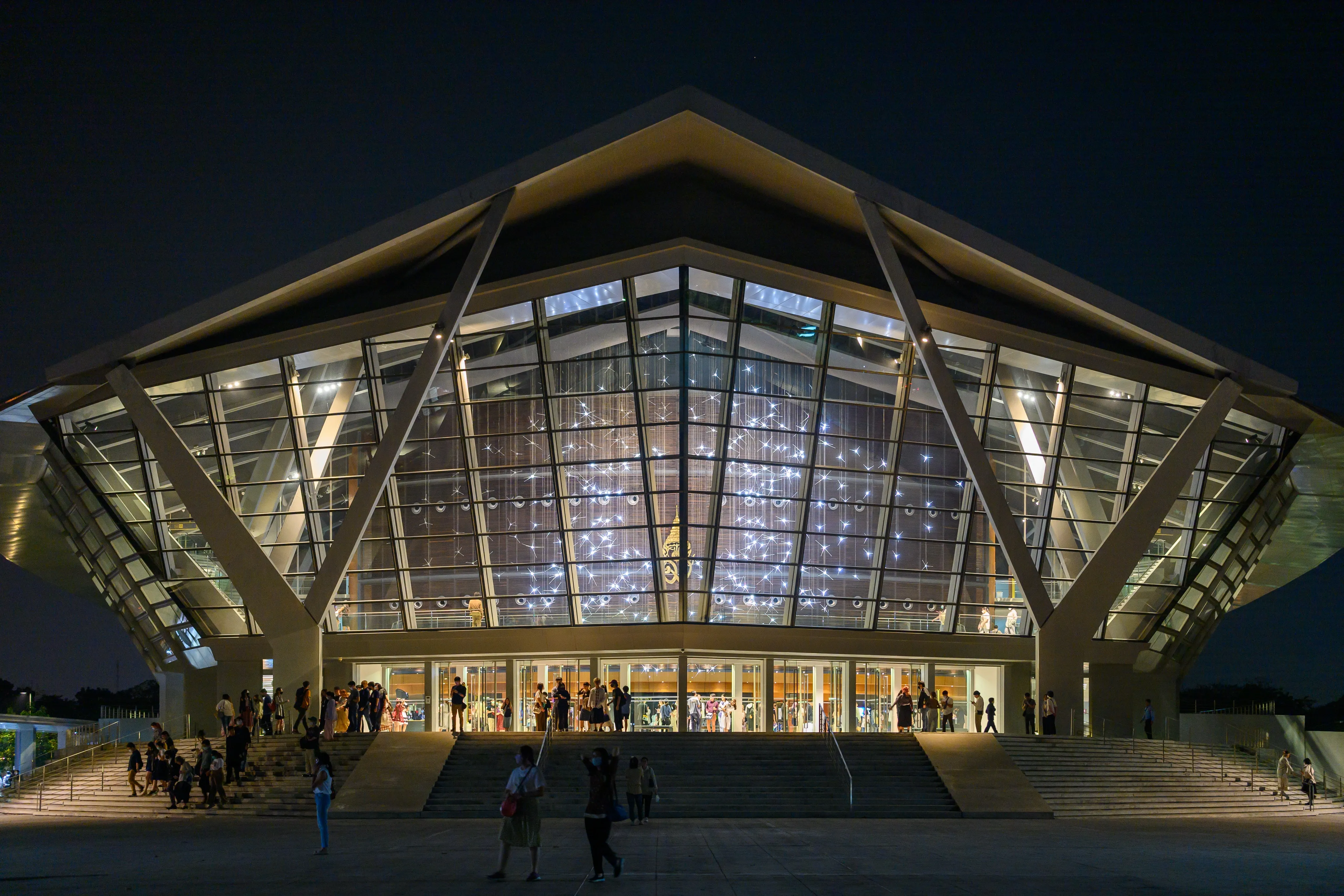 A brightly lit glass building with a broad angular roof at night
