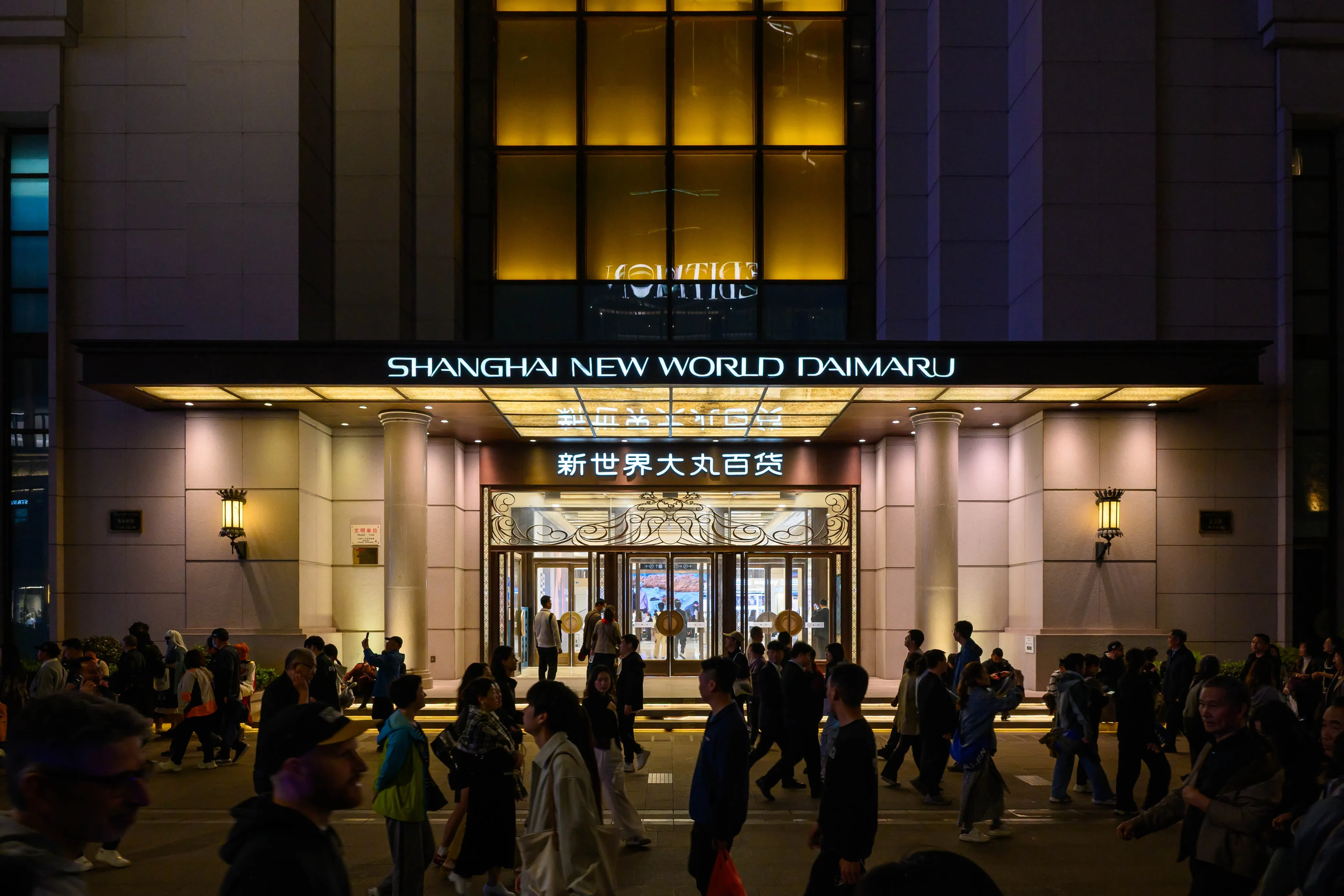 People outside the illuminated Shanghai New World Daimaru entrance