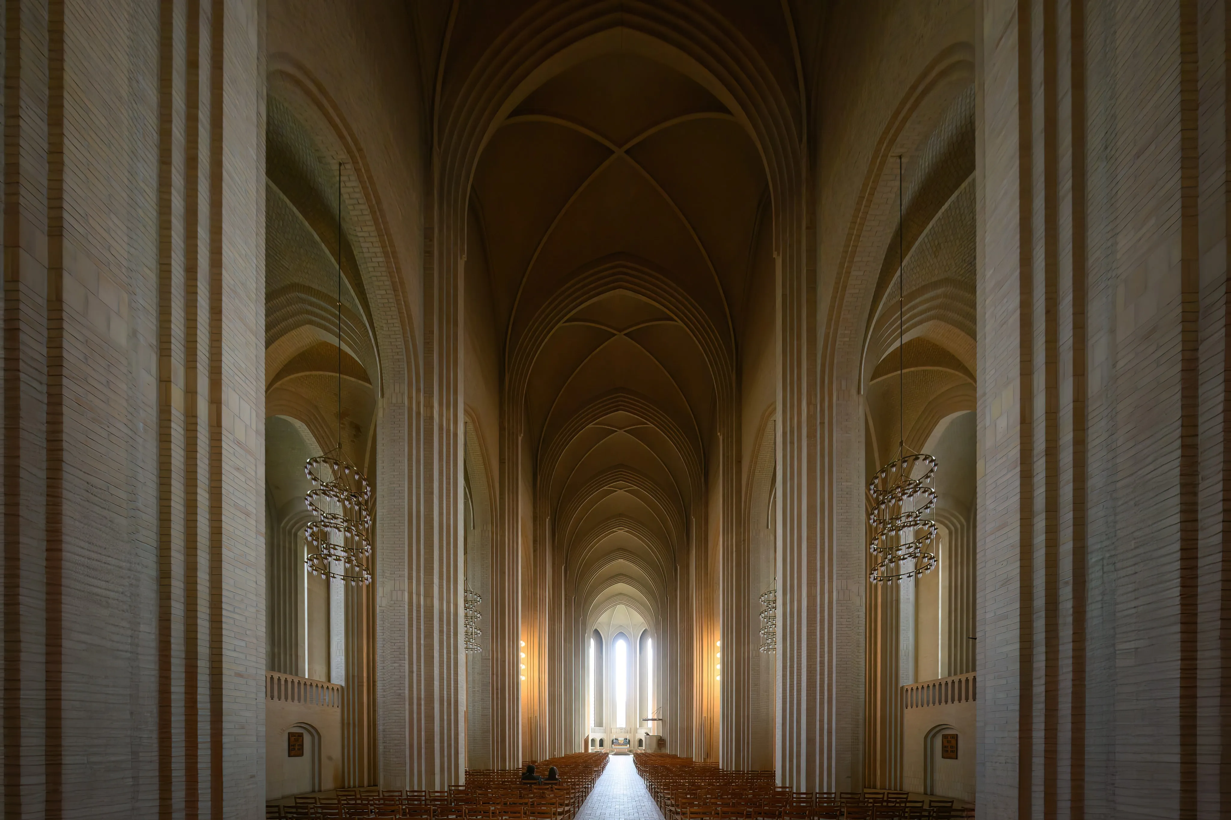 Tall brick arches leading toward a sunlit church window