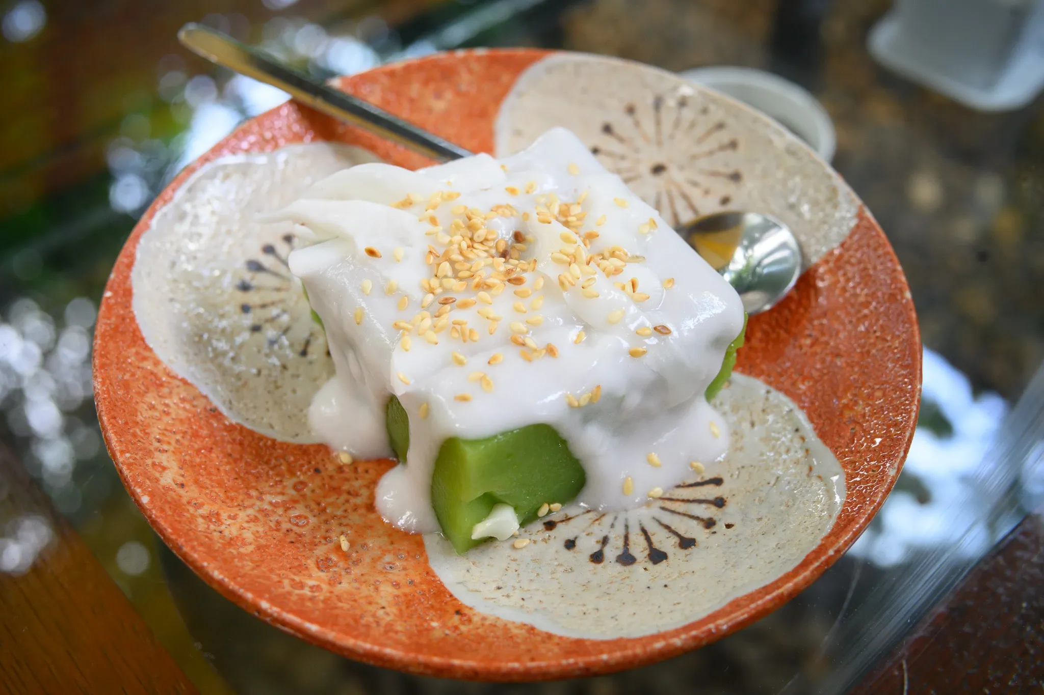 A green pandan dessert covered in coconut cream and sesame on a patterned plate