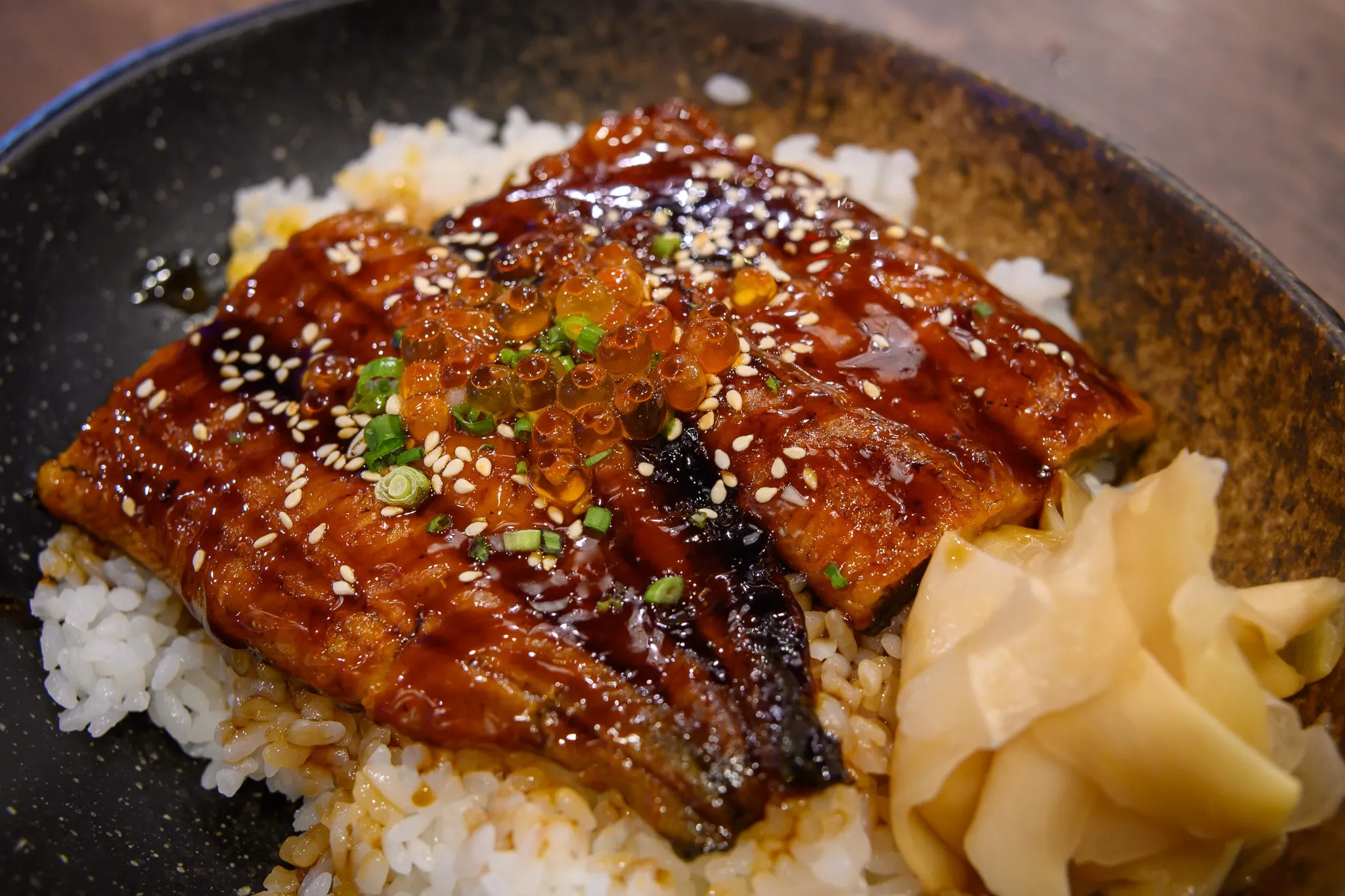 Glazed grilled eel with sesame and roe over rice, with pickled ginger