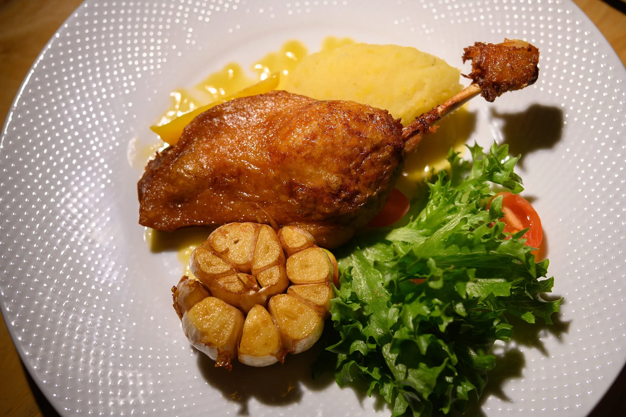 Duck confit with roasted garlic, mashed potato, and salad greens on a white plate