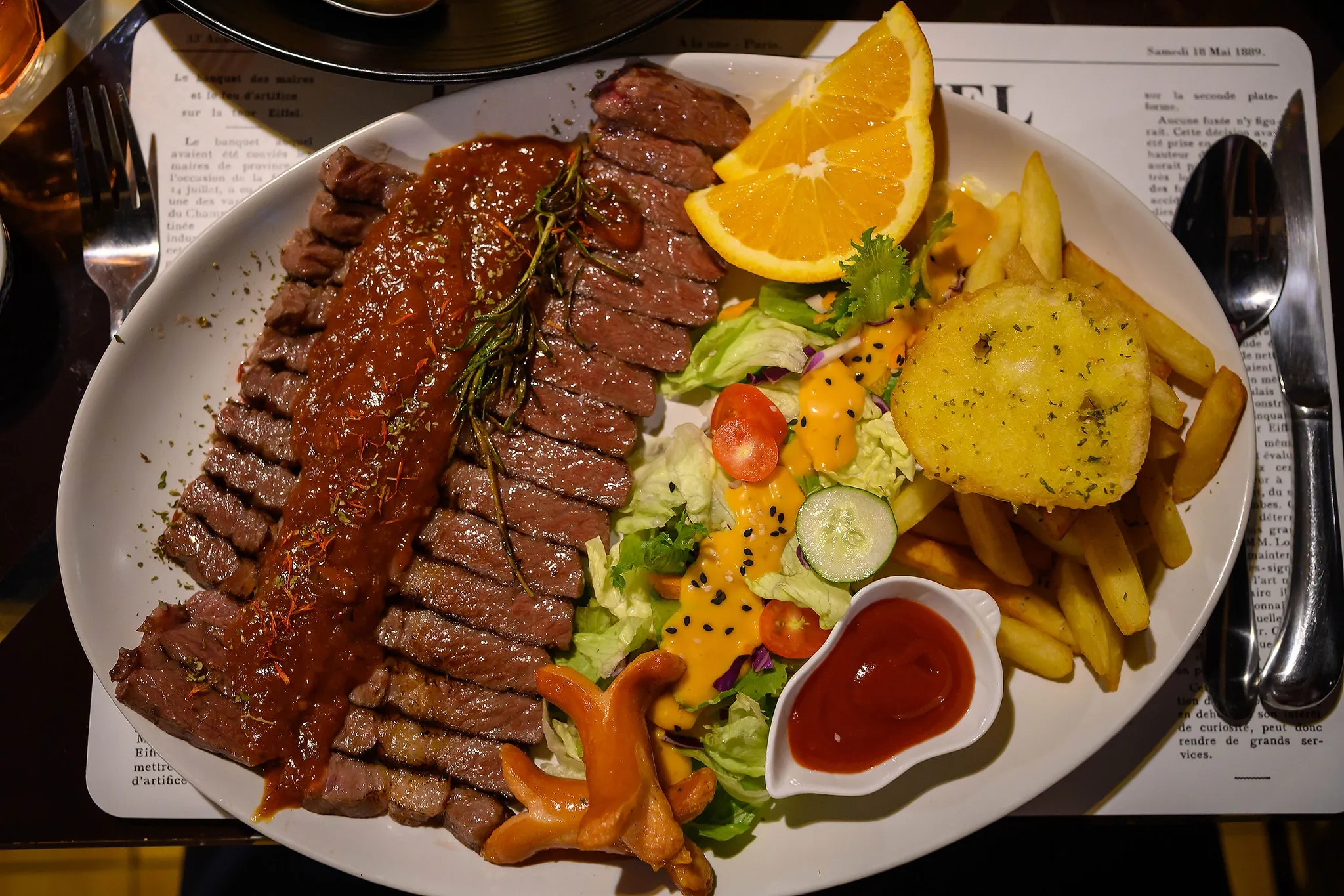 Sliced steak served with potatoes, vegetables, fries, and orange wedges