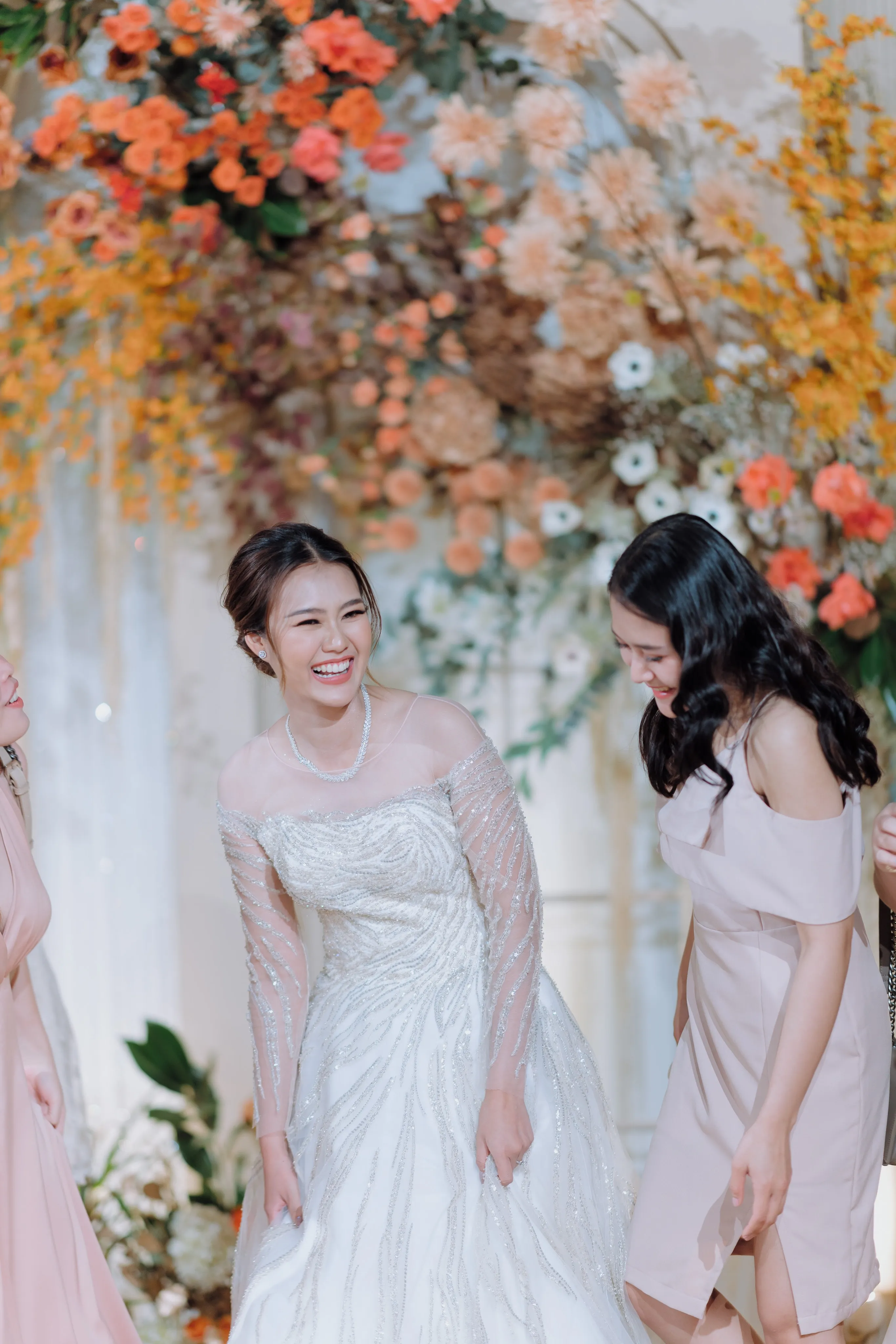 The laughing bride with a bridesmaid in front of an orange-and-white floral backdrop