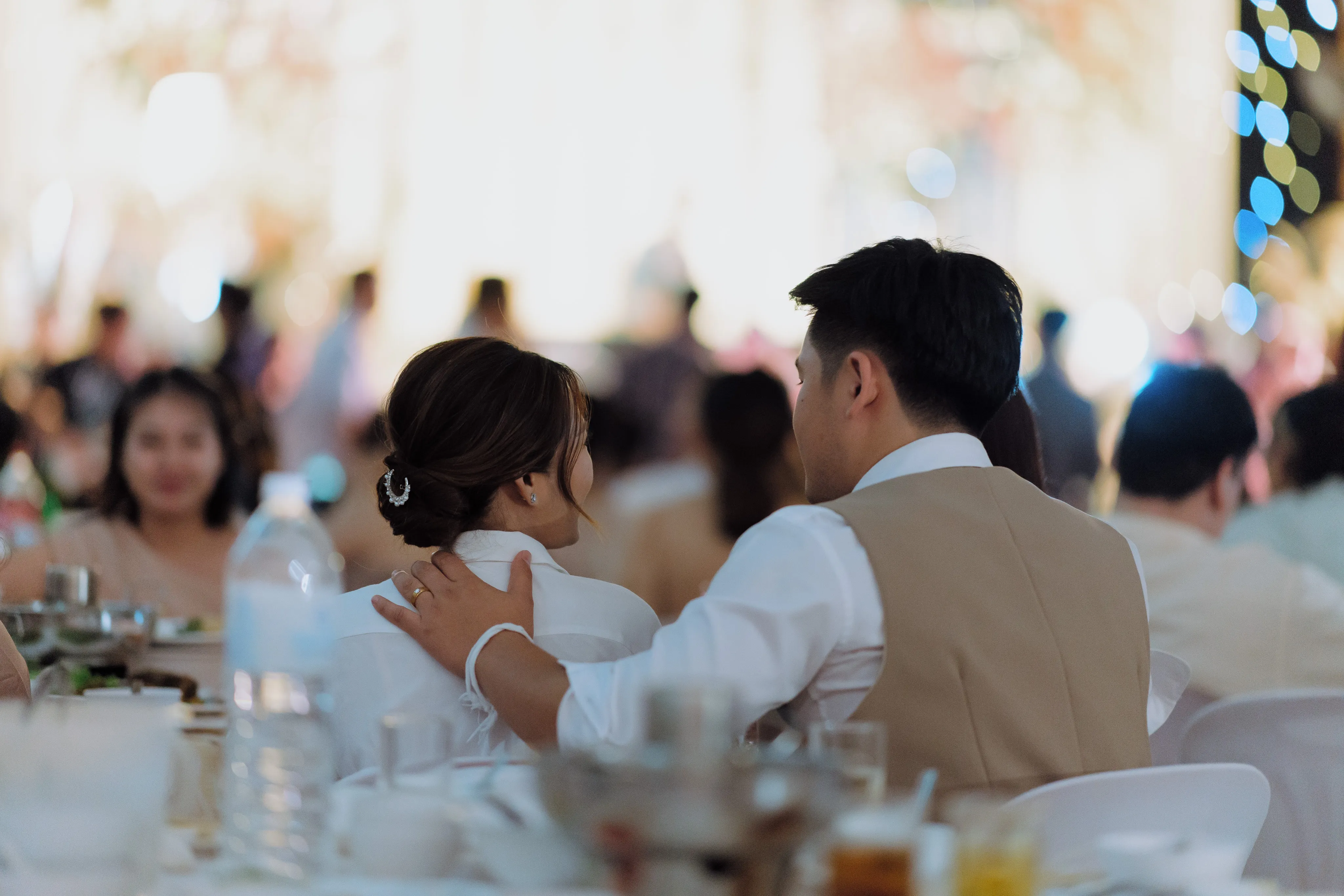The bride and groom seen from behind with their arms around each other at a reception table